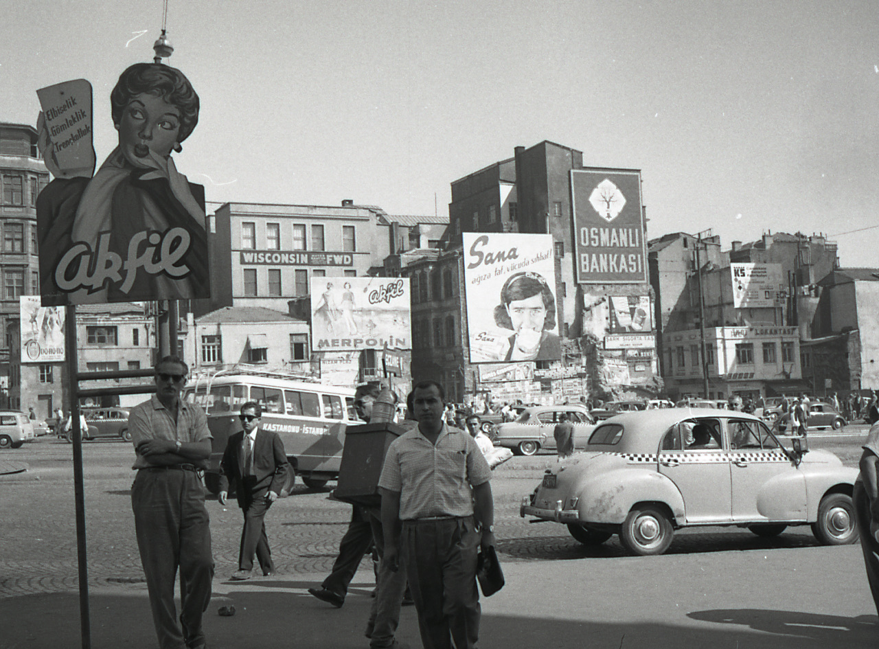 1962'de İstanbul'da kalabalık bir meydanda minibüs, taksi ve yayalar, arka planda dönemin reklam panoları